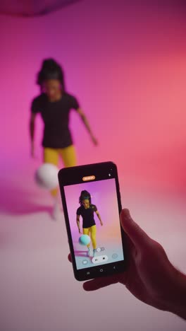 Vertical-Video-Studio-Shot-Of-Female-Footballer-Recording-Video-For-Social-Media-On-Mobile-Phone-Teaching-Ball-Skills